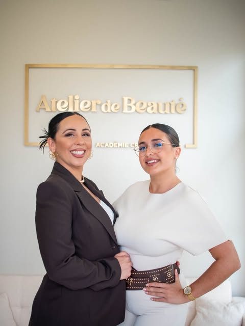 Dos profesionales del atelier posando juntas delante del rótulo dorado de la marca.